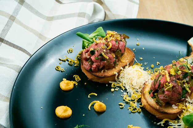 Tartaar van rundvlees op gebakken croutons geserveerd op een stijlvolle zwarte plaat. Restaurant eten.