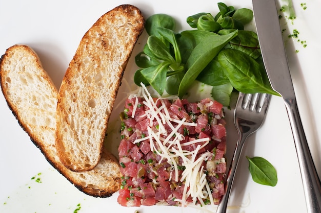 Tartare di manzo con spinaci su un piatto bianco.