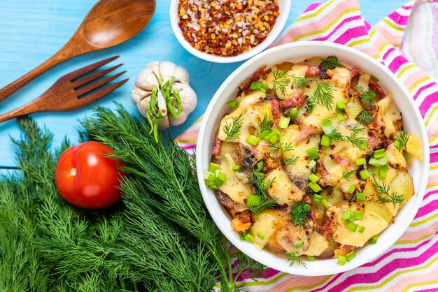 Tartiflette with bacon, herbs and vegetables over wooden blue table. Top view.