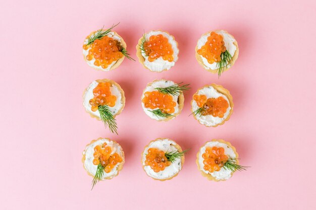 Tartlets filled with red caviar and cream cheese on a pink surface. Appetizer with sea delicacies.