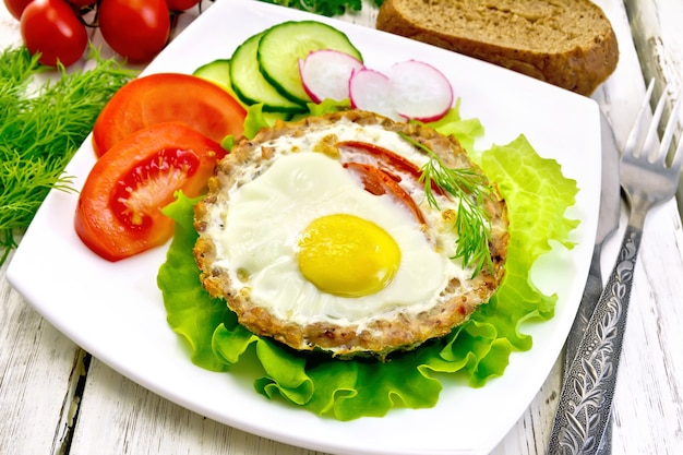 Мясные тарталетки с яйцом и помидорами в тарелке на листьях салата, хлебе и укропе на фоне светлых деревянных досок