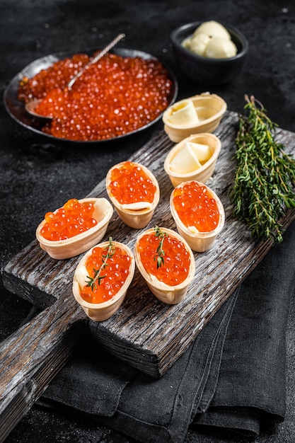 Tartlets met rode kaviaarboter en tijm op een houten bord Zwarte achtergrond Bovenaanzicht