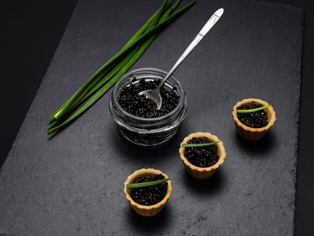 Tartlets with black sturgeon caviar and green onions on a slate plate