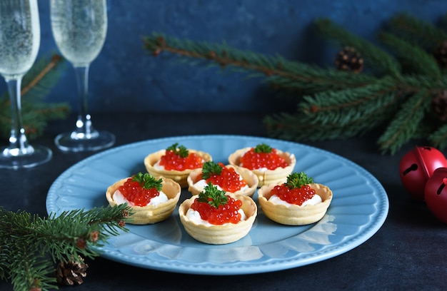 Tortine con crema di formaggio e caviale rosso su un bel piatto sulla tavola di natale.