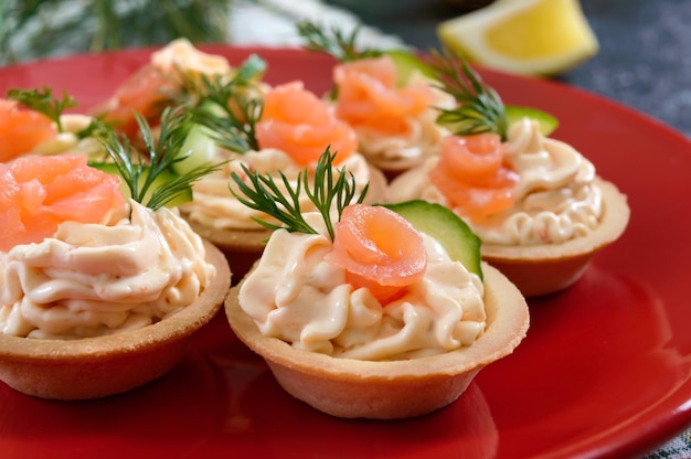 Tartellette con crema di formaggio e salmone salato su un piatto rosso. spuntino leggero e gustoso per una festa. cibo da mangiare con le mani. avvicinamento