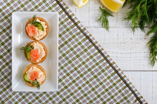 Tortine con crema di formaggio e salmone salato su un piatto bianco. spuntino leggero e gustoso per una festa. cibo da mangiare con le mani. la vista dall'alto, distesa.