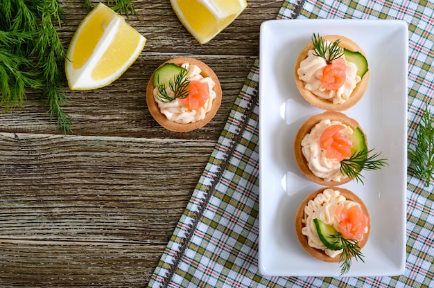 Tartlets with cream cheese and salted salmon on a white plate. Tasty light snack for a party. Finger Food.