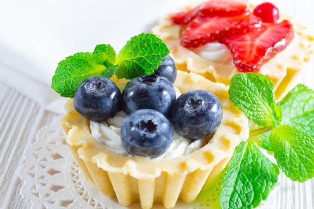 Tartlets with fresh blueberries, strawberries and cream cheese on white wooden background.