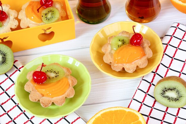 Tartlets with fruits and tea on a white wooden table