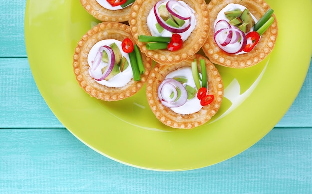 Tartlets with greens and vegetables with sauce on plate on table