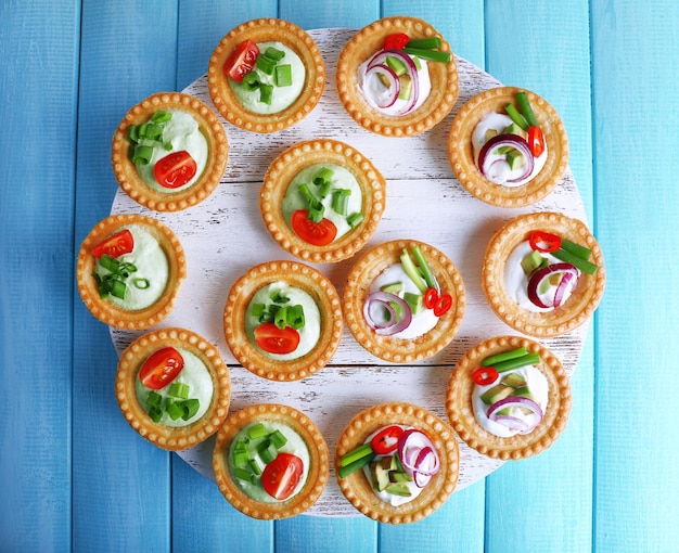 Tartlets with greens and vegetables with sauce on tray on table