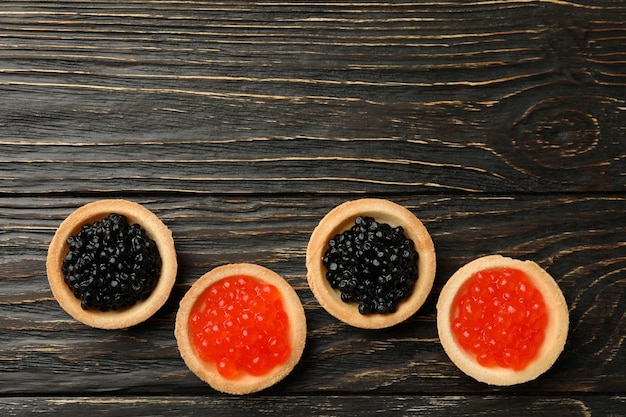 Tartlets with red and black caviar on wooden background, top view