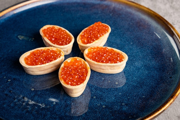 Tartlets with red caviar and butter on a blue plate closeup