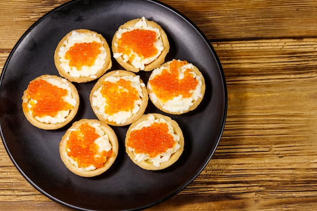 Tartlets with red caviar and soft cheese on a wooden table Top view