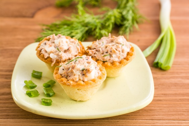 Tartlets with salad on a saucer and fresh herbs on a wooden table