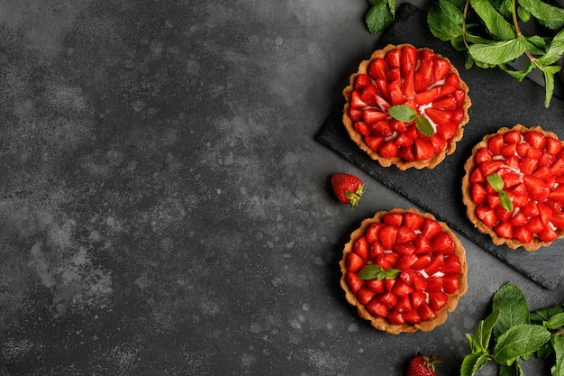 Tarts with Strawberries cream and mint on slate board and dark background Cake basket dessert