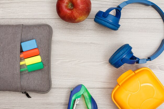 Tas-etui met kleurviltstiften en marker, appel, nietmachine, koptelefoon en lunchbox.