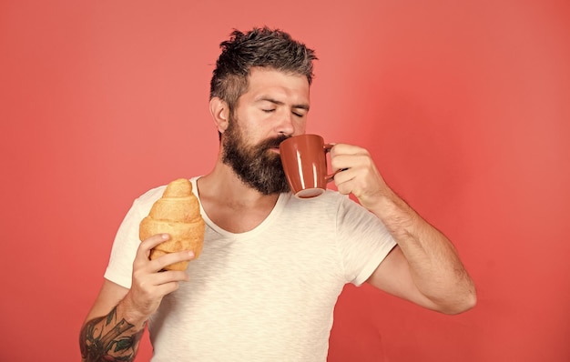 Taste it Unhealthy but yummy breakfast Perfect match feel hunger Bearded hipster enjoy breakfast drink coffee Morning tradition concept Fresh baked croissant Delicious breakfast