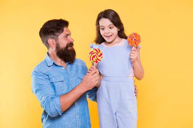 Taste the rainbow family of father and daughter eat candies\
happy family yellow background bearded man entertain little child\
with treats family time love and trust fun thing family do\
together