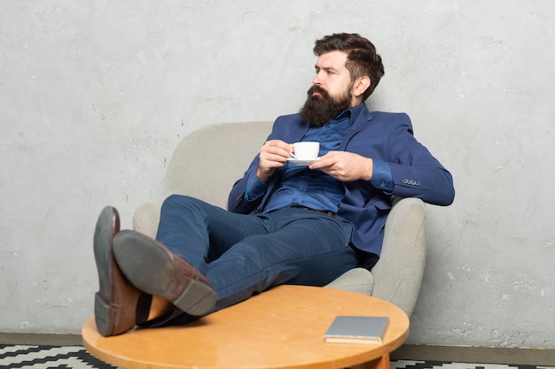 Taste of relaxation. Lawyer drink tea in armchair. Bearded man have break sitting feet up. Tea break. Relax and have rest time.