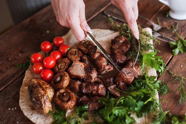 Tasting piece of shishkebab preparing on barbecue grilled meat field mushrooms and cherry tomatoes