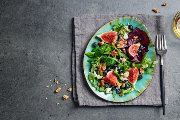 Tasty appetizing autumn salad with figs blueberries cheese nuts and arugula served on plate on dark background.