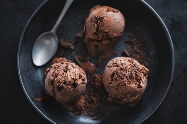 Photo tasty appetizing chocolate ice cream with chocolate chunks on dark plate on dark background.