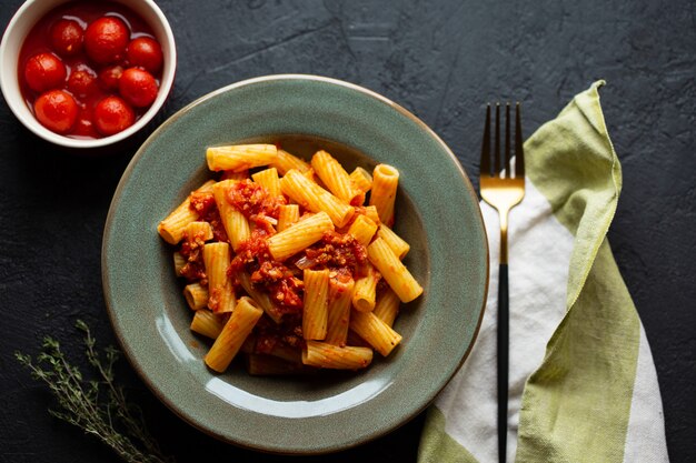 Вкусные аппетитные классические итальянские макароны с томатным соусом, сыром пармезан и лапшой на тарелку на темном столе. Вид сверху, горизонтальный. Итальянские макароны. Паста Пенне в томатном соусе с курицей, помидорами.