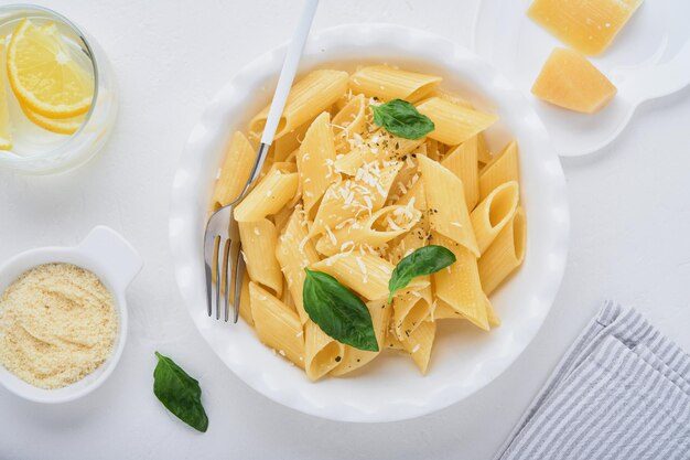 写真 石のテーブルの上のプレートに白いプレートのパルメザンチーズとバジルを添えたおいしい食欲をそそる古典的なイタリアのペンネパスタ。イタリア料理の伝統料理。上面図。