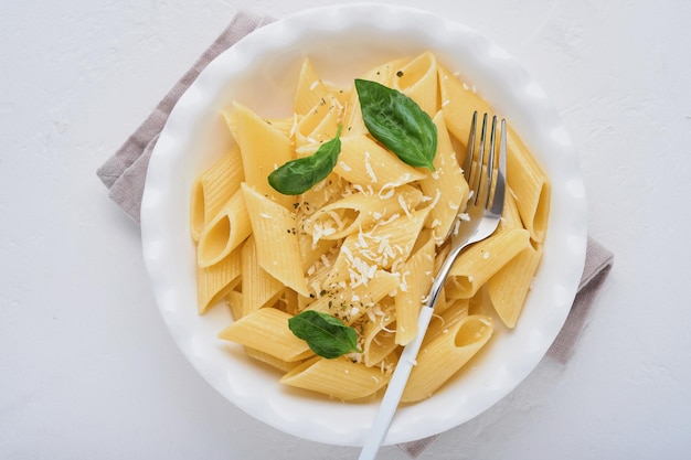 Tasty appetizing classic italian penne pasta with parmesan cheese and basil in white plate on plate on on stone table. Traditional dish of Italian cuisine. Top view.
