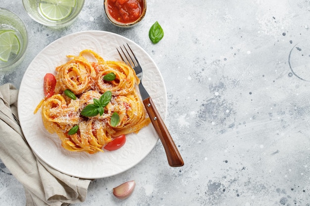 Tasty appetizing classic italian tagliatelle pasta with tomato sauce, cheese parmesan and basil on plate on light table. View from above, horizontal. Top view with copy space