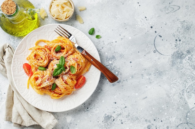 Tasty appetizing classic italian tagliatelle pasta with tomato sauce cheese parmesan and basil on plate on light table View from above horizontal Top view with copy space