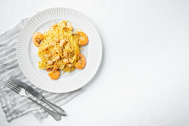 Tasty appetizing pasta spaghetti with pesto sauce and shrimps set, on plate, on white stone surface, top view flat lay, with copy space