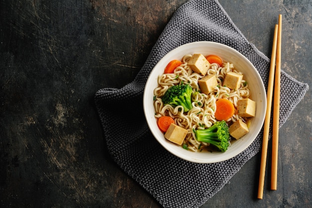 두부, 국수와 야채가 들어간 맛있는 식욕을 돋우는 채식주의 아시아 수프가 콘크리트 표면에 그릇에 담겨 있습니다.