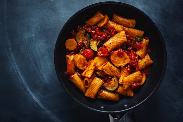 Tasty appetizing vegetarian pasta with vegetables and tomato sauce served on pan. Top View.