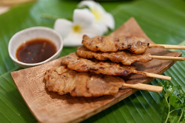 Tasty asian grilled pork on skewer on a wooden plate with\
traditional asian sauce asian street food