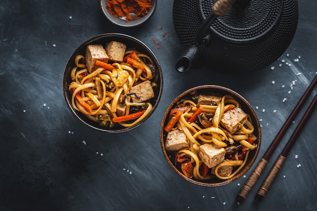 Tasty asian noodles with cheese tofu and vegetables on plates.