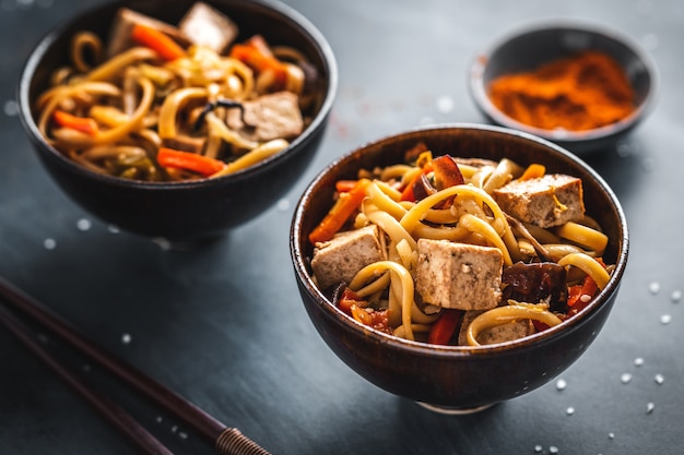 Tasty asian noodles with cheese tofu and vegetables on plates.