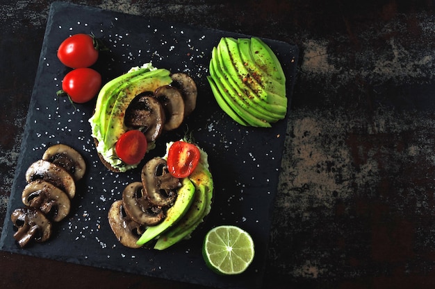 Tasty avocado toasts with mushrooms and cherry tomatoes, served on a stone board.