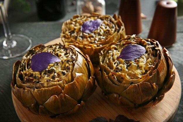 Tasty baked artichokes on round wooden board close up