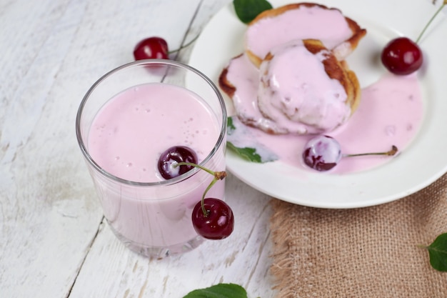 Tasty beautiful pancakes in a white plate with cherry and yogurt in a glass cup on a light wooden table with mint leaves.