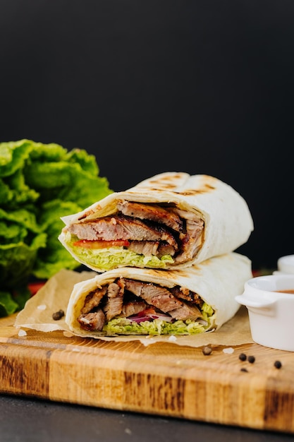 Tasty beef shawarma with fresh salad and vegetables lying on wooden board traditional arab dishes