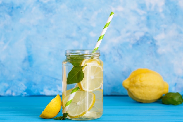 Tasty beverage with lemon and basil in glass jar on blue background