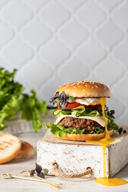 Tasty big burger with lettuce cutlet cheese vegetables and egg with leaking egg yolk on white kitchen tile background Text space
