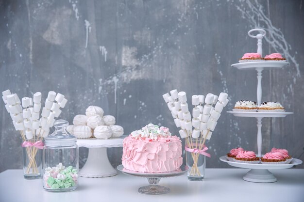 Photo tasty birthday cake and sweets on table against grunge wall