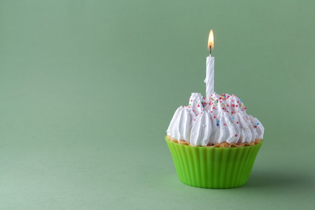 Tasty birthday cupcake with candle, on green background