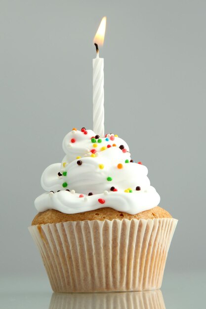 Tasty birthday cupcake with candle on grey background