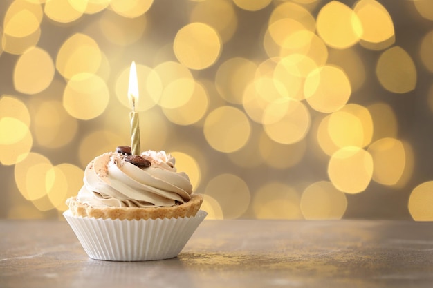 Tasty birthday cupcake with candle on table against blurred lights space for text