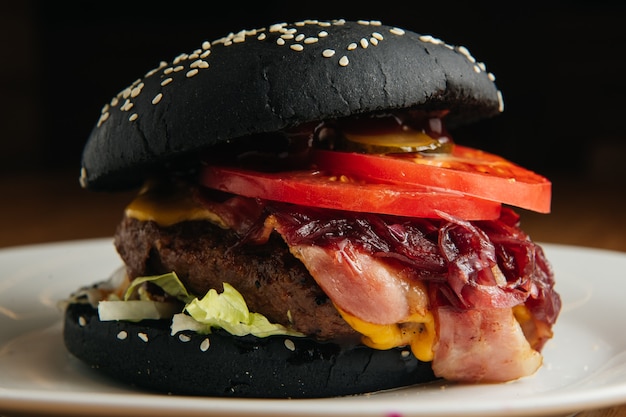 tasty black burger with bacon on white plate