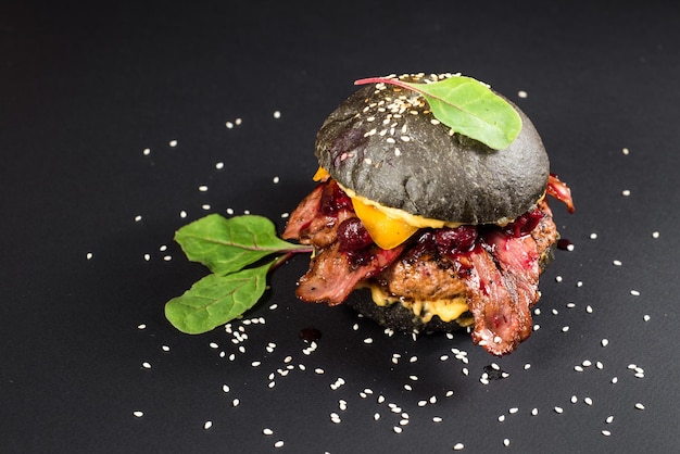 Tasty black burger with meat, bacon, cheese and cherry on the black background